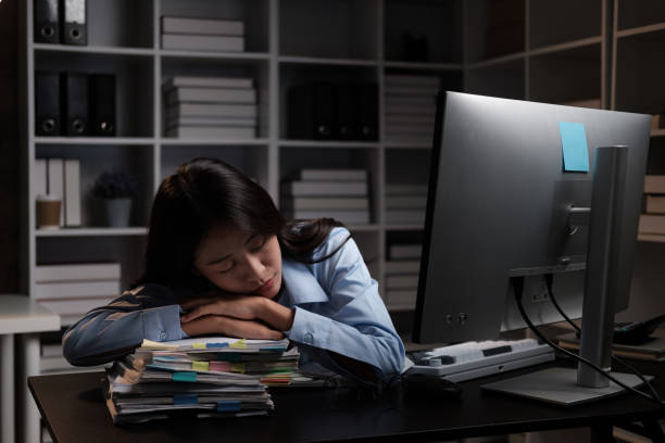 istock Tired Asian businesswoman taking a nap on her table while working overtime at night. 1572349335
