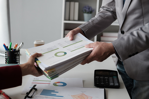 Close up view of businessman handing work document to his boss, working in the office room.