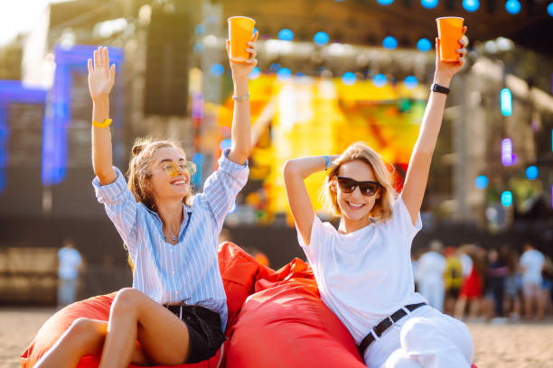 istock Two young girlfriends have fun with beer at the beach party. 1572368822