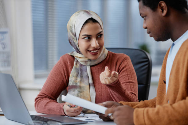 istock Happy young businesswoman in headscarf explaining working point 1572377948