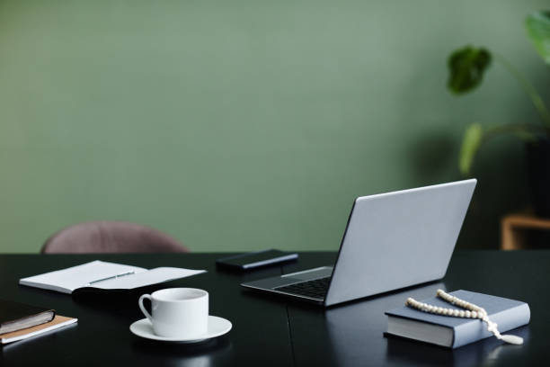 istock Office workplace desk with open laptop against green wall 1572378486