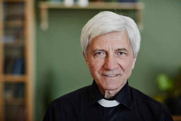 istock Close up white haired senior priest smiling at camera in office setting 1572379030