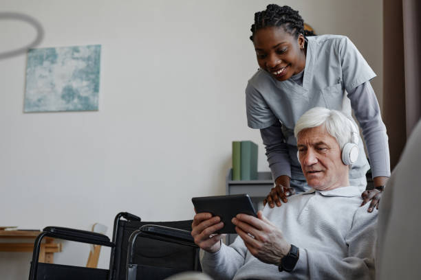 istock White haired senior man with disability relaxing at home with nurse assisting 1572379625