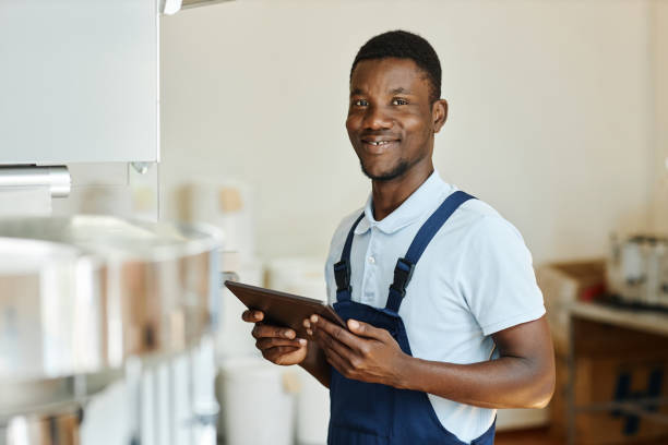 istock Young black factory worker holding tablet and smiling at camera 1572383905