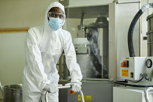 Portrait of black man wearing mask and protective suit working with chemicals at pharmaceutical factory, copy space