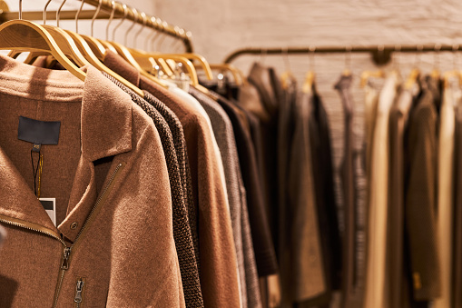 Warm toned background image of coats on rack in clothing store, copy space