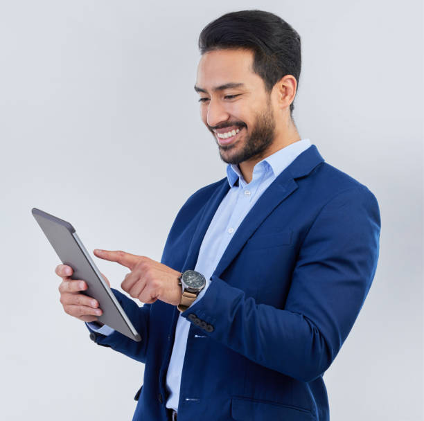 istock Smile, tablet and asian businessman in studio reading email, networking and internet on white background. Connect, online report and man in suit, communication and technology for investor at startup. 1572396222