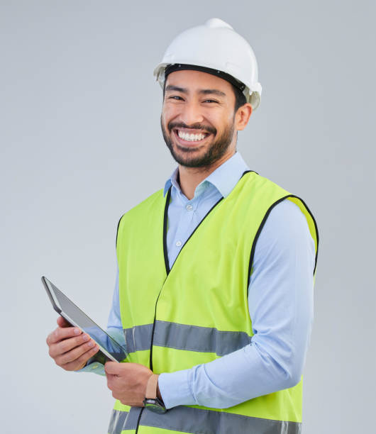 istock Construction worker, portrait and happy man in studio with tablet and helmet safety on white background. Smile, internet and contractor or architect in online planning for project management in India 1572410516