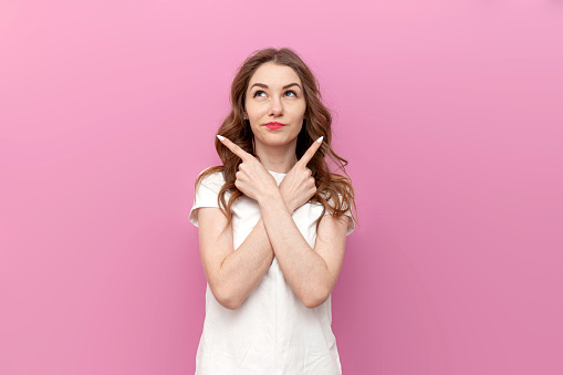 young cute woman chooses from two options and shows with her hands to both sides on pink isolated background, thoughtful girl puzzled by difficult choice