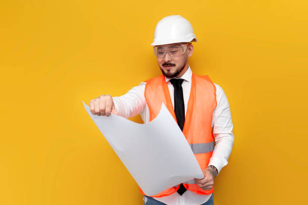 istock asian foreman in uniform with papers and projects on yellow isolated background, korean civil engineer in hardhat 1572420525