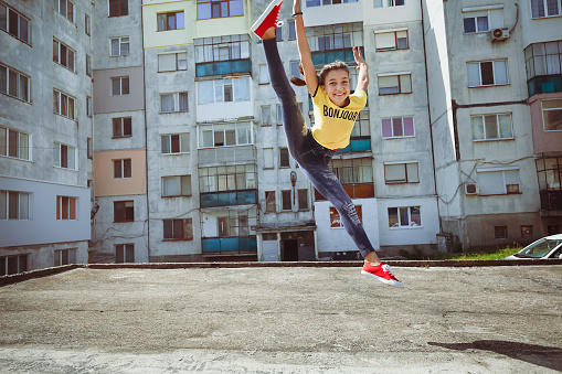 Happy teenage girl jumping and dancing in front of apartment building. Summer fun. Hanging around the neighborhood. Training outside.
