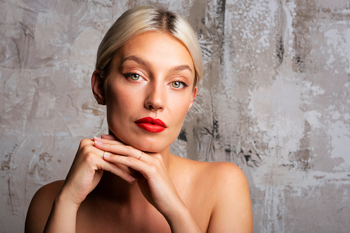 Close-up studio portrait of attractive blond haired woman wearing red lipstick and standing at isolated background.