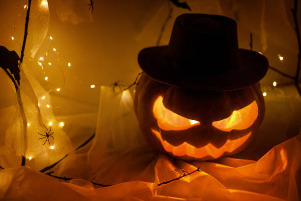 istock Spooky Jack o lantern carved pumpkin, spider web, ghost, bats and glowing light in dark. Scary atmospheric halloween party decorations, space for text. Happy Halloween! Trick or treat 1572480871