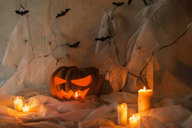 istock Happy Halloween! Spooky Jack o lantern carved pumpkin, spider web, ghost, bats and glowing light in evening. Scary atmospheric halloween party decorations, space for text. Trick or treat 1572483101