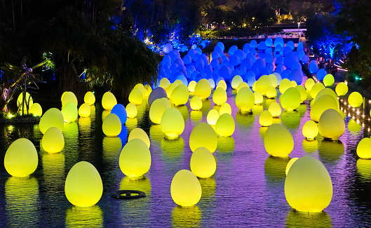 Singapore - Feb 25, 2020. Colorful neon blue and yellow eggs float on water surface of Dragonfly lake in Gardens by the bay in twilight. Temporary event called Future Together created by Japanese art teamLab.