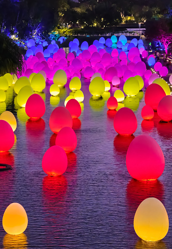 Singapore - Feb 25, 2020. Colorful blue, pink, red and yellow eggs float on water surface of Dragonfly lake in Gardens by the bay in twiglight. Temporary event called Future Together created by Japanese art teamLab. Vertical shot