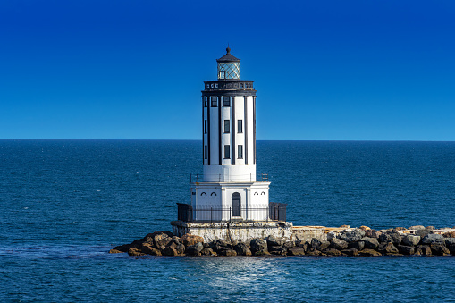 beautiful, old lighthouse, red white and sailboat in bright sunshine, blue sky and blue water