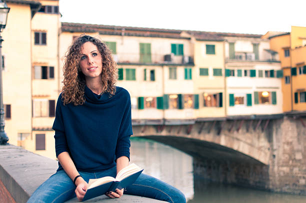 High angle shot of a young woman on a park bench eating a croissant and drinking coffee during a reading break