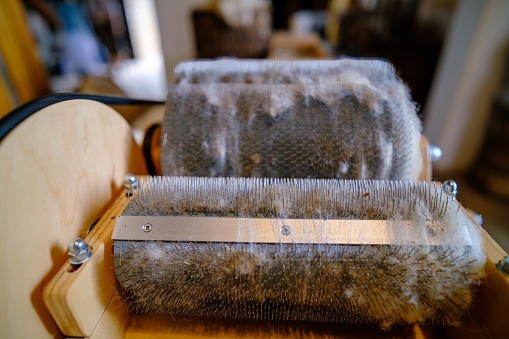 Wool felting. The step of combing the material in a special carding machine. Focus on foreground.