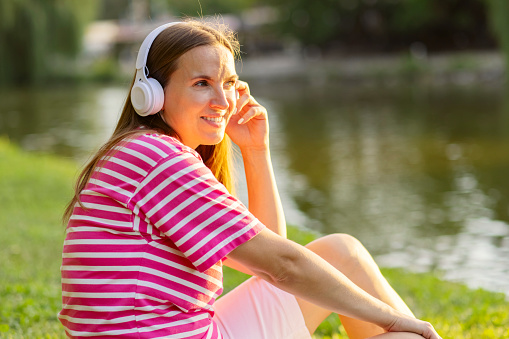 Beautiful woman enjoy listening to music with headphones feeling happy and relaxed in the park