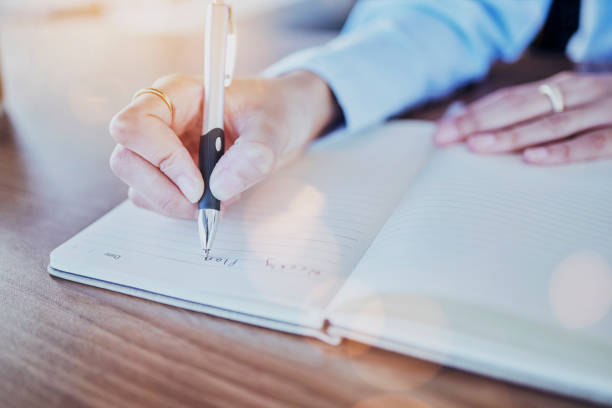 istock Notebook, pen and hands writing ideas, planning schedule and research notes for start up business idea. Journal, brainstorming and commitment, hand of woman writer on diary or note on project plan. 1572553565