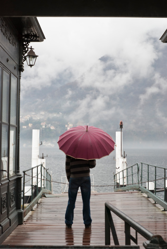 Lonely man standing with umbrella under the rain in Cernobbio harbour, Lake Como. 