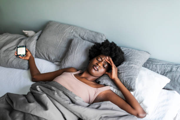 istock Beautiful young black woman with relationship difficulties lying down in bed with mobile 1572576605