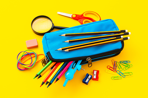 Pencil case full of colored school supplies shot on yellow background.