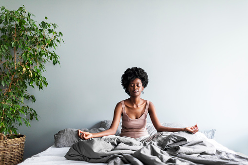 Young black woman sitting in lotus in the morning in bed