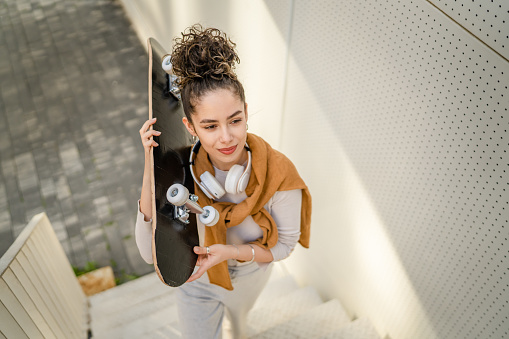 One woman young adult caucasian teenager stand outdoor with skateboard on her shoulder posing portrait happy confident real person copy space