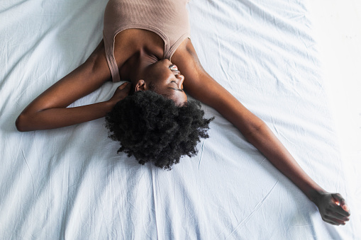 Young adult black woman waking up stretching and yawning