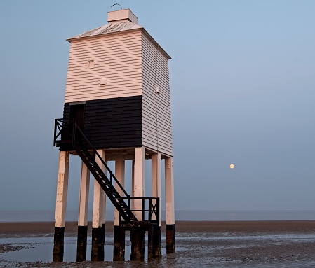 three quarters view of Burnham-on-Sea Low Lighthouse at sunrise sunset with full moon in background
