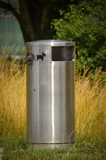 A silver metal trash can on the side of the road