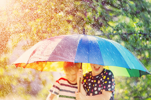 Boy and girl standing outdoors in rainy day under colourful umbrella. Concept of the friendship and childhood.