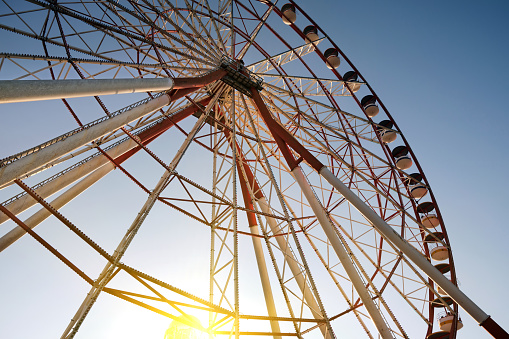 Bottom view of a large Ferris wheel attraction on the background of the sunset sky.