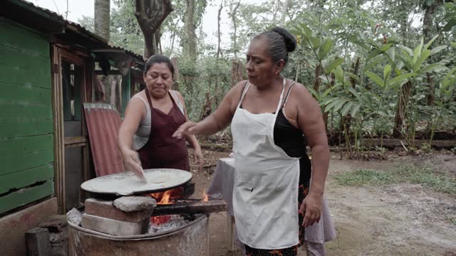 Two adult Hispanic women are shaping corn tortillas by hand