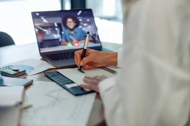 Photo of Close up of woman freelancer have video conference with client and making notes sitting near window