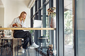 Smiling business woman working on laptop, making notes in cozy coworkign space interior