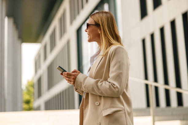 istock Woman manager with phone standing on modern building background and looking at side 1572733467