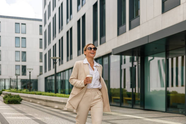istock Smiling woman entrepreneur with coffee walking on modern building background during break time 1572734530