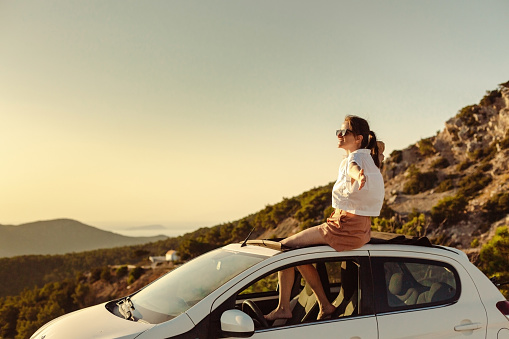 Shot of a woman enjoying a relaxing road trip. She is taking a break from a car drive and enjoying the sunset