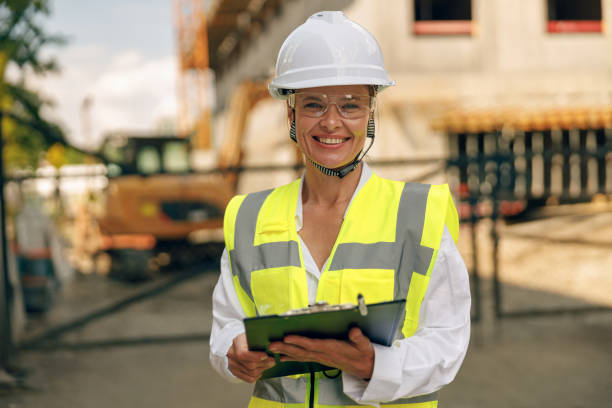 istock Female engineer in protective helmet making notes on construction site and looking at camera 1572741375