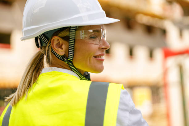 istock Smiling female construction worker in protective helmet standing against on construction background 1572741386