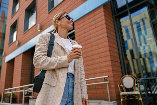 Smiling business woman drinking coffee during break time near office building. High quality photo