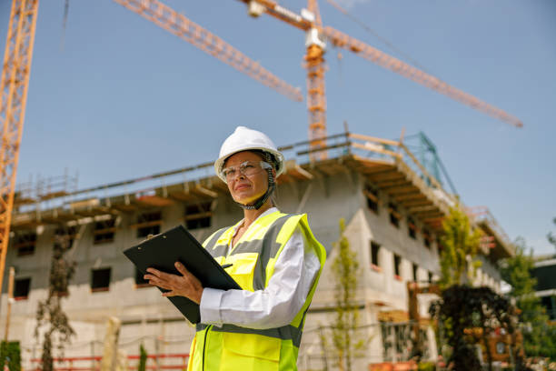 istock Smiling female construction worker in protective helmet standing against on construction background 1572758032