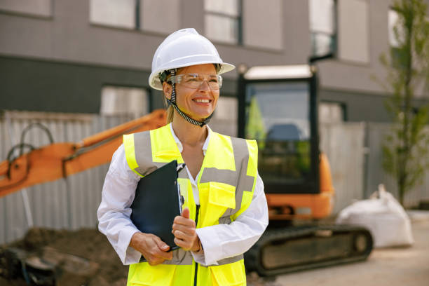 istock Smiling female construction worker in protective helmet standing against on construction background 1572758033