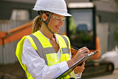 Professional female engineer in protective helmet making notes on construction site
