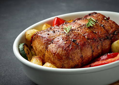 bowl of whole roast pork and vegetables on dark grey kitchen table