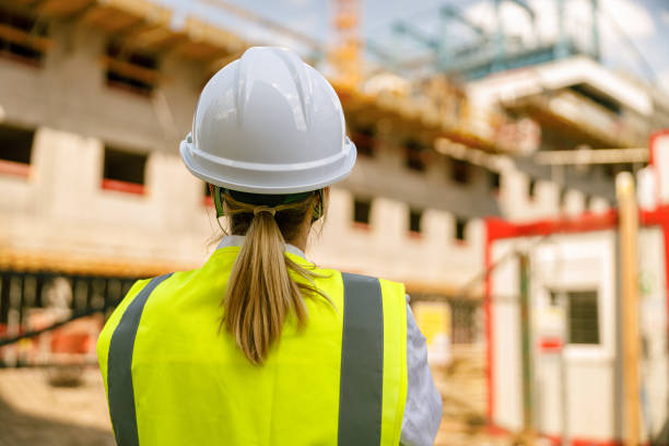 istock Back view of female construction worker in protective helmet against on construction background 1572779345