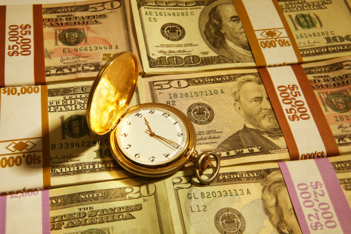 Gold pocket watch on a background of thousands of dollars wrapped neatly in bunches.